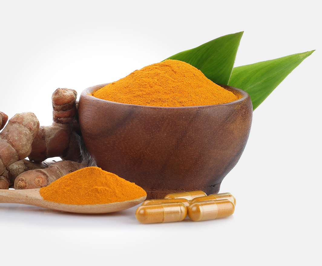 A wooden bowl filled with curcumin sits beside a spoon, five Ultra Cur tablets, and fresh ginger.